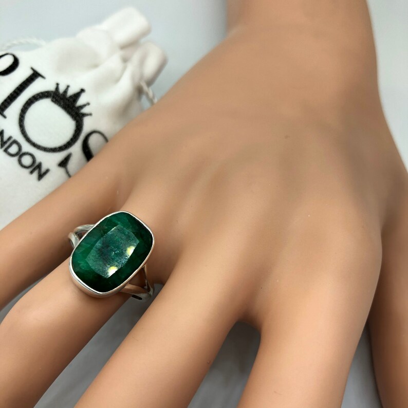 May include: A silver ring with a large, rectangular, emerald green gemstone. The ring is on a mannequin hand.