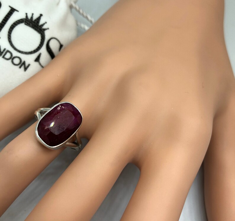 May include: A silver ring with a large, rectangular, dark red gemstone. The ring is on a hand.