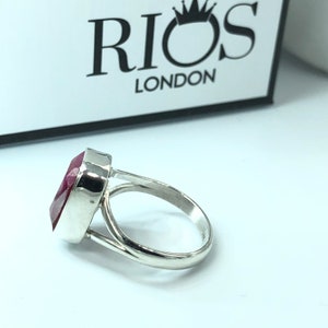 May include: A silver ring with a large, red gemstone. The ring is set in a simple, elegant design. The ring is made by Rios London.