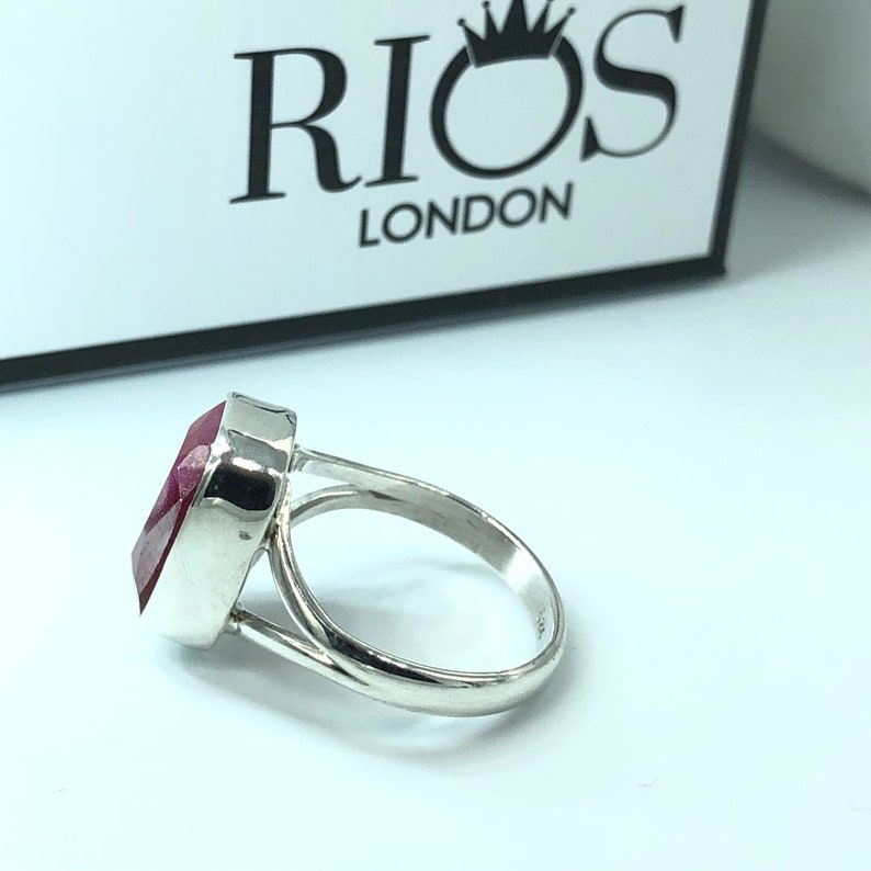 May include: A silver ring with a large, red gemstone. The ring is set in a simple, elegant design. The ring is made by Rios London.