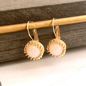 Op de afbeelding: Een paar gouden oorbellen met witte opaalstenen. De oorbellen hebben een delicaat, ingewikkeld ontwerp en zijn perfect om elke outfit een vleugje elegantie te geven.