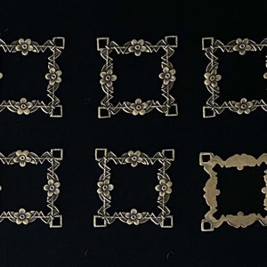 May include: Seven antique gold-toned metal square frames with ornate floral designs. The frames are approximately 1 inch in size.