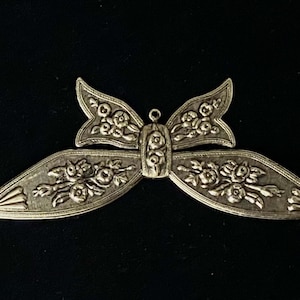 May include: A silver-toned metal butterfly charm with a floral design. The butterfly has a loop at the top for attaching to a necklace or bracelet.