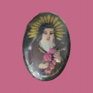 May include: Oval-shaped, silver-toned pendant with a colorful image of a woman in a brown robe holding pink flowers. The woman has a halo of yellow rays around her head.