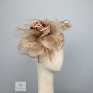 K&ouml;nnte beinhalten: Eine gro&szlig;e, beige Stoffrose mit einer kleineren, dunkleren Rose in der Mitte. Die Rose befindet sich auf einem Mannequin-Kopf.