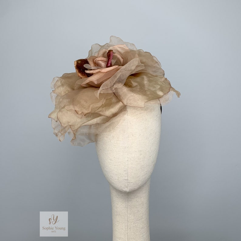 K&ouml;nnte beinhalten: Ein zartes, rosafarbenes Stoffblumen-Haarschmuckst&uuml;ck mit einem mehrschichtigen, gekr&auml;uselten Design. Die Blume besteht aus durchsichtigem Stoff und hat eine leicht strukturierte Oberfl&auml;che.