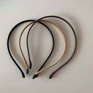 Puede incluir: Tres diademas finas en negro, beige y marr&oacute;n. Cada diadema tiene un dise&ntilde;o simple y redondeado con una punta negra o marr&oacute;n en cada extremo. Las diademas est&aacute;n dispuestas en un patr&oacute;n ligeramente superpuesto sobre un fondo blanco liso.