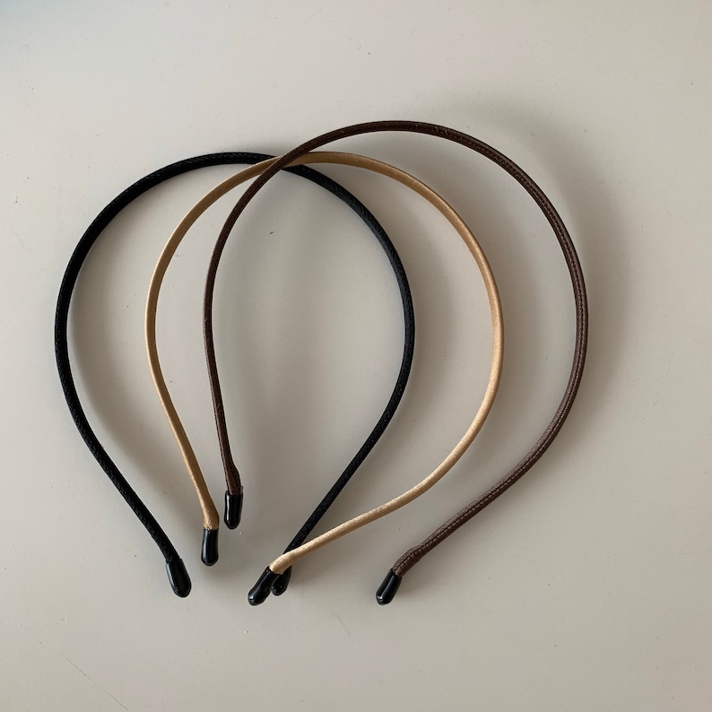 Puede incluir: Tres diademas finas en negro, beige y marr&oacute;n. Cada diadema tiene un dise&ntilde;o simple y redondeado con una punta negra o marr&oacute;n en cada extremo. Las diademas est&aacute;n dispuestas en un patr&oacute;n ligeramente superpuesto sobre un fondo blanco liso.