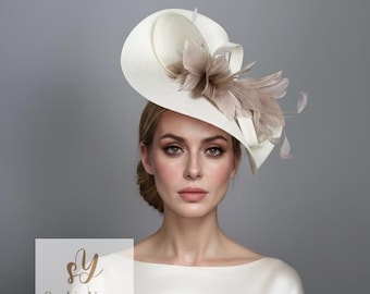 Könnte beinhalten: Ein cremeweißer Fascinator-Hut mit einer breiten, geschwungenen Krempe und einem Büschel hellbrauner Federn. Der Hut wird schräg getragen und enthält den Text Sophie Young HATS in der unteren linken Ecke des Bildrahmens.