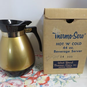 May include: A gold and black Thermo-Serv beverage server with a 44 ounce capacity. The server is in its original box, which reads "Hot 'N' Cold Beverage Server" and "West Bend Thermo-Serv, Inc. Anoka, Minn."