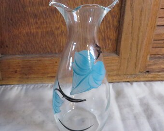 May include: A clear glass vase with a ruffled top and a blue floral design. The vase is hand-painted with black outlines and blue flowers.