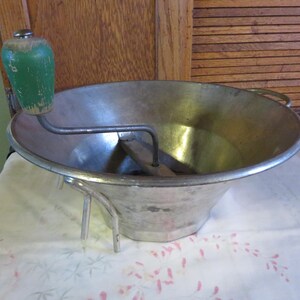 May include: A vintage silver food mill with a green wooden handle. The mill has three legs and a crank handle.