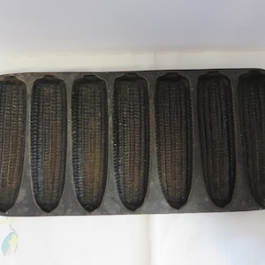May include: A vintage cast iron cornbread pan with eight individual molds. The pan is dark gray and has a slightly worn surface.