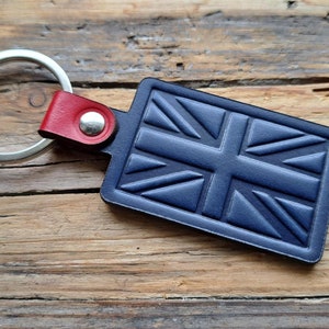 Puede incluir: Un llavero de cuero azul con un dise&ntilde;o de Union Jack y un anillo de llave plateado. El llavero tiene una correa de cuero roja con un remache plateado.