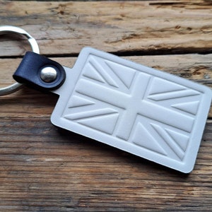 Puede incluir: Un llavero plateado con una correa de cuero y un dise&ntilde;o de Union Jack blanco en relieve.