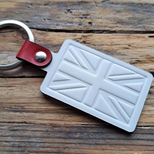 Puede incluir: Llavero de cuero blanco con un anillo de llave plateado y una correa de cuero roja. El llavero presenta un dise&ntilde;o de Union Jack en relieve.