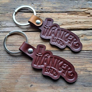 May include: Two brown leather keychains with silver key rings. Each keychain features the text "Wanker Bar" in a stylized font with a small illustration of a top hat above the text.