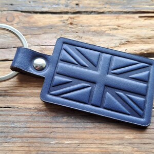 Puede incluir: Un llavero de cuero azul con un anillo de llave plateado y un dise&ntilde;o de Union Jack en relieve.