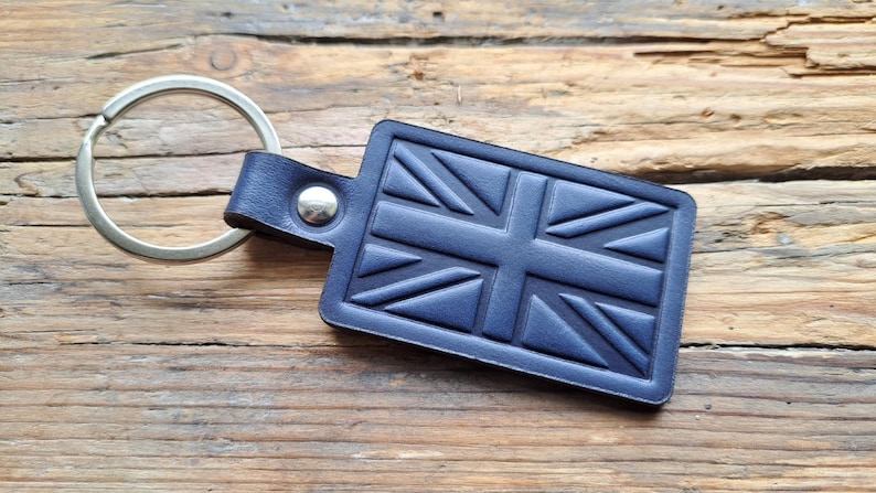Puede incluir: Un llavero de cuero azul con un anillo de llave plateado y un dise&ntilde;o de Union Jack en relieve.