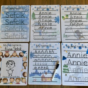 May include: Six dry-erase boards with winter-themed illustrations. The boards are designed for children to practice writing their names. The boards feature a snowman, a penguin, a house, and a winter landscape. The text on the boards includes "My first name is...", "My last name is...", "My full name is...", and "My name is...".