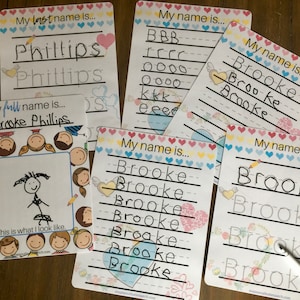 May include: A set of six colorful dry-erase boards with a heart border. Each board has a different activity for learning to write a name. The boards include the name "Brooke" written in cursive and printed, as well as the last name "Phillips".