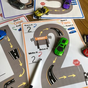 K&ouml;nnte beinhalten: Eine druckbare Lernaktivit&auml;t f&uuml;r Kinder mit einer Rennstrecke in Form der Zahl Zwei, auf der ein gr&uuml;nes Spielzeugauto f&auml;hrt. Die Aktivit&auml;t enth&auml;lt Anweisungen zum Nachzeichnen, Schreiben, Buchstabieren, Z&auml;hlen und Fahren der Zahl Zwei.