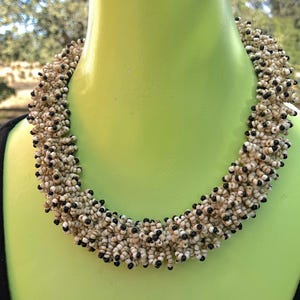 May include: A white and black beaded necklace with a chunky, layered design. The necklace is made of small, round beads and is approximately 16 inches long.