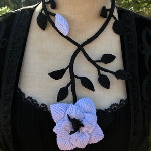 May include: A black macrame necklace with a delicate vine design and a large, light purple flower pendant.
