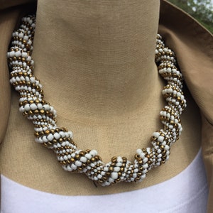 Puede incluir: Un collar de cuentas blancas y doradas con un diseño en espiral.