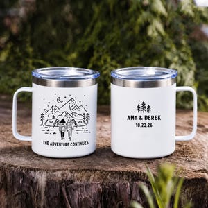 May include: Two white stainless steel mugs with clear lids and handles. One mug features a black line art graphic of two people camping under mountains and stars with the text THE ADVENTURE CONTINUES. The other displays three trees, AMY & DEREK, and 10.23.26.