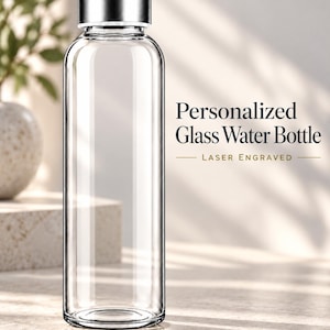 Peut inclure: Une bouteille d'eau en verre transparent avec un corps cylindrique et un bouchon à vis en métal argenté. Le texte Personalized Glass Water Bottle LASER ENGRAVED est visible à droite de la bouteille en lettres noires et dorées.