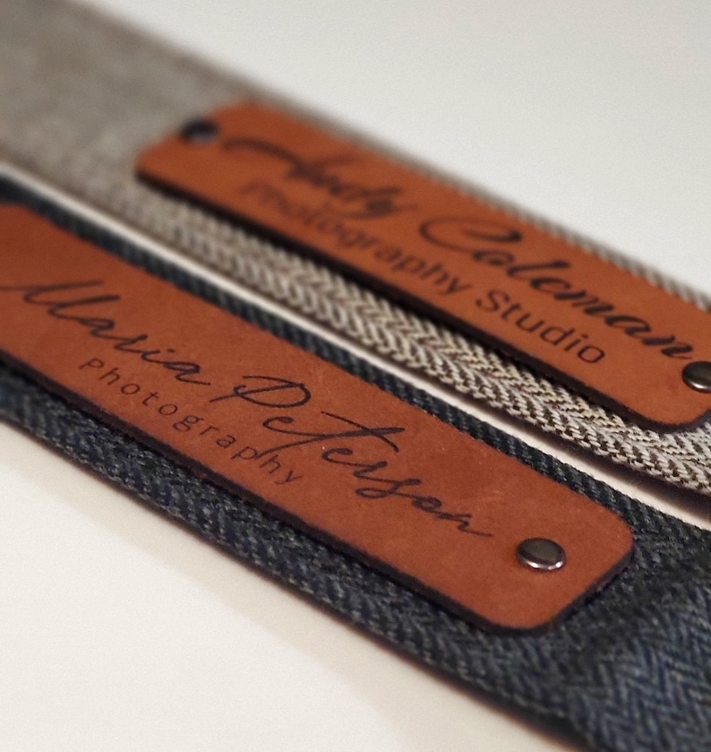May include: Two brown leather camera straps with metal rivets. The straps are personalized with the names "Maria Peterson Photography" and "Holly Coleman Photography Studio".