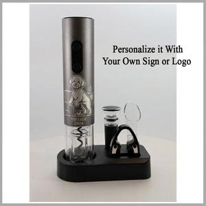 Könnte beinhalten: Ein silberner elektrischer Weinöffner mit einer Hundeillustration und dem Text "VINTAGE 2024". Der Öffner steht auf einer schwarzen Basis mit Zubehör. Der Text auf dem Bild lautet "Personalisiere es mit deinem eigenen Zeichen oder Logo".