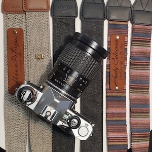 May include: Four camera straps with different patterns and colors. The straps are made of fabric and leather. The straps have metal buckles and are adjustable. The straps have personalized name tags with the text "Maria Peterson Photography" and "Andy Coleman Photography Studio".