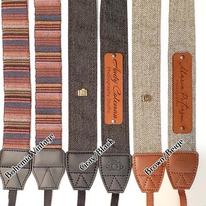 May include: Four camera straps with different patterns and colors. The straps are made of woven fabric and have leather ends. The straps have personalized leather tags with the names "Andy Coleman Photography Studio" and "Maria Peterson Photography".