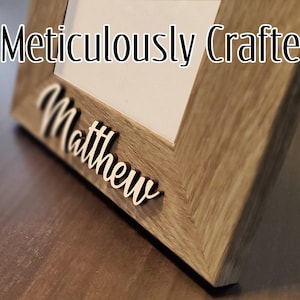 Könnte beinhalten: Ein Holzbildrahmen mit hellbrauner Oberfläche. Der Rahmen hat einen weißen Passepartout und eine weiße Aufschrift mit dem Text "Meticulously Crafted". Der Name "Matthew" ist in weißen Buchstaben auf der Unterseite des Rahmens geschrieben.