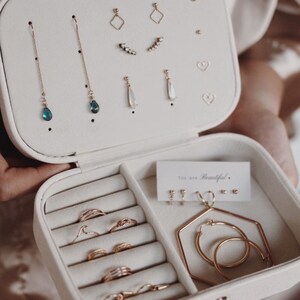 May include: White jewelry box with compartments for earrings, rings, and necklaces. The box has a velvet lining and a gold clasp. The text "You are Beautiful." is printed on a small card inside the box.