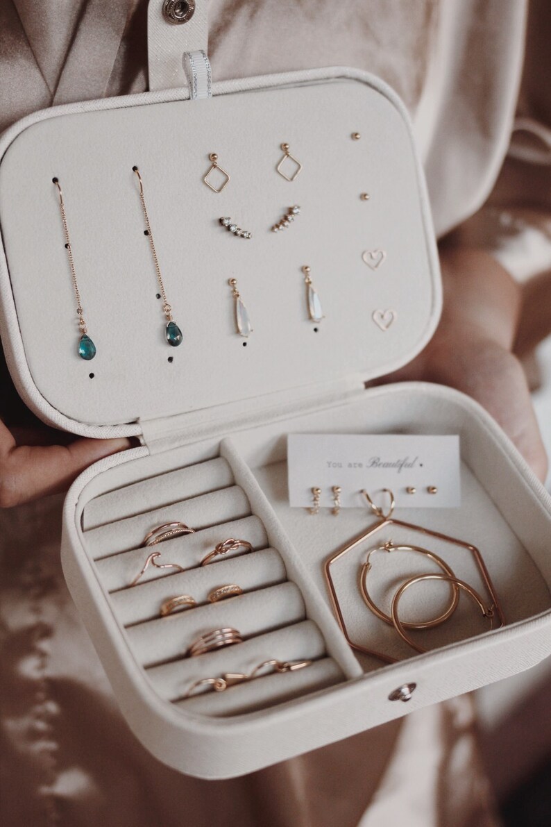 May include: White jewelry box with compartments for earrings, rings, and necklaces. The box has a velvet lining and a gold clasp. The text "You are Beautiful." is printed on a small card inside the box.