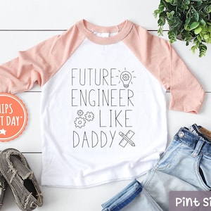 May include: A white and pink baseball tee shirt with the text "Future Engineer Like Daddy" and a lightbulb, gears, and a pencil and ruler graphic.