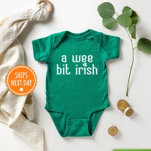May include: A green baby onesie with white text that reads "a wee bit irish" and a shamrock.