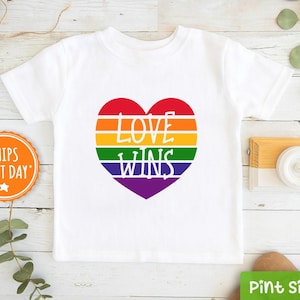 May include: White t-shirt with a rainbow heart that says "LOVE WINS" in white text.