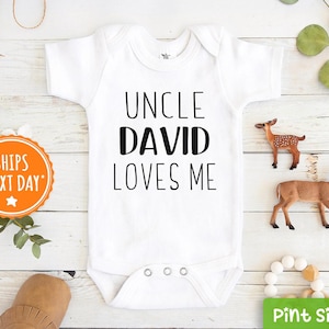 May include: White baby onesie with black text that reads "Uncle David Loves Me".