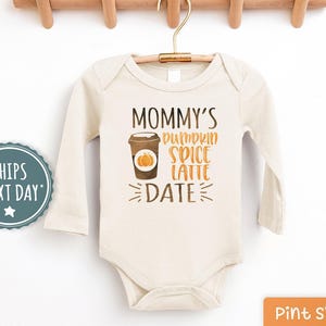 May include: A beige long-sleeved bodysuit with the text "Mommy's Pumpkin Spice Latte Date" and a graphic of a cup of coffee with a pumpkin on it.