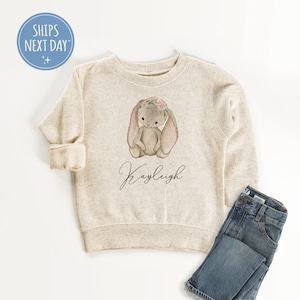 May include: A beige sweatshirt with a brown bunny wearing a flower crown and the name "Kayleigh" printed on the front.