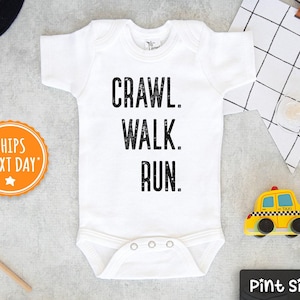 May include: White baby onesie with black text that reads "Crawl. Walk. Run."