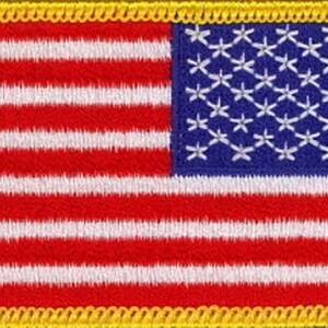 May include: A small embroidered American flag patch with a yellow border. The flag is red, white, and blue with 13 stripes and 50 stars.