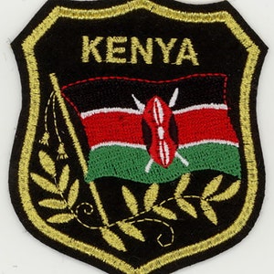 May include: Embroidered patch with a black background and gold trim. The patch features the Kenyan flag with a spear and shield, a gold branch, and the word "KENYA" in gold lettering.