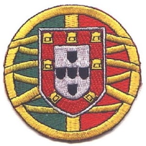 May include: A circular embroidered patch with a yellow border, green and red background, and a white and black coat of arms in the center.