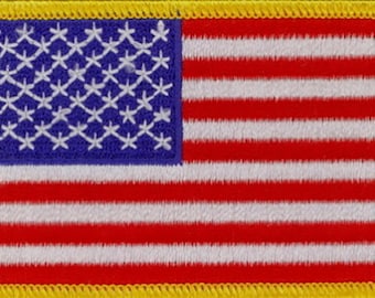 May include: Embroidered patch featuring the American flag. The design includes a blue canton with white stars and red and white stripes. The patch is bordered with a yellow fringe.