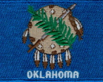 May include: Embroidered patch featuring the Oklahoma state seal on a blue background. The seal includes a shield, olive branch, and Native American symbols. The word "OKLAHOMA" is embroidered in white at the bottom.